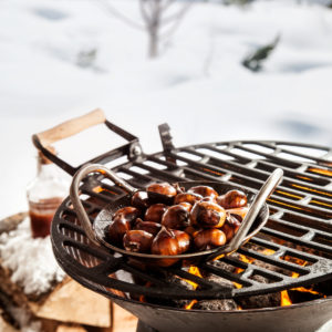 Dish of roasted chestnuts on a barbecue grilling over the hot coals outdoors in a snowy winter landscape ready for a winter BBQ party